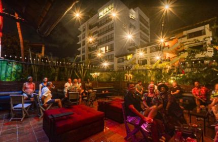 Night view of a gay bar in Puerto Vallarta, Mexico. People are seated in an outdoor patio with red cushions and string lights.
