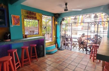 Anonimo Gay Bar in Puerto Vallarta, Mexico. Colorful bar interior with stools, open patio, and two men sitting outside. Gay travel.