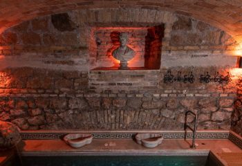 Apollion Sauna Rome: Interior view of the sauna, featuring a stone wall with a bust in a niche, and a small pool. Gay travel advice.