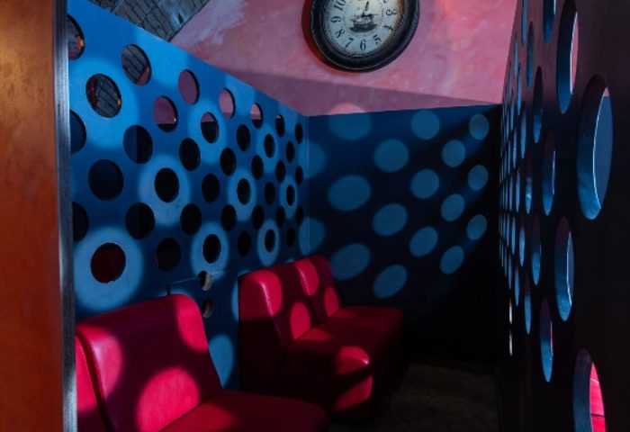 Apollion Sauna Rome: Interior view with red seats, blue walls with circular cutouts, and a clock. Gay sauna travel advice.