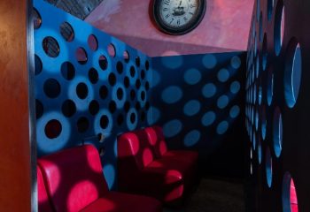 Apollion Sauna Rome: Interior view with red seats, blue walls with circular cutouts, and a clock. Gay sauna travel advice.