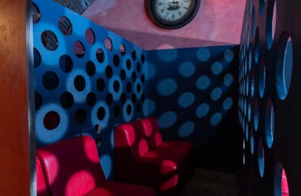 Apollion Sauna Rome: Interior view with red seats, blue walls with circular cutouts, and a clock. Gay sauna travel advice.