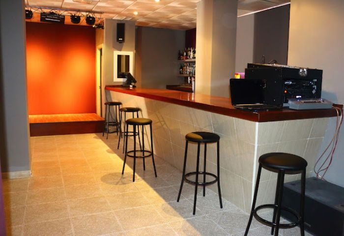 Bar area inside Apolo Cabaret, a gay sauna in Torremolinos. Stools line the bar, with a stage area visible in the background.
