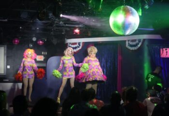 Aqua Bar Key West gay party: Drag queens perform on stage at a nightclub. Disco ball and crowd visible. Gay travel advice.