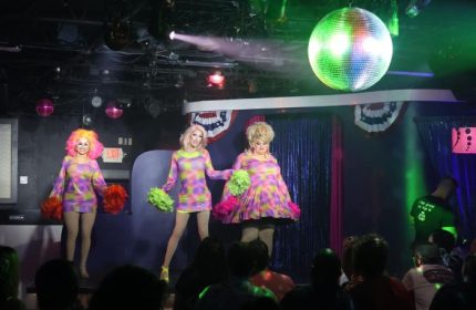 Aqua Bar Key West gay party: Drag queens perform on stage at a nightclub. Disco ball and crowd visible. Gay travel advice.