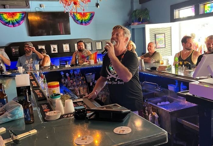 Aqua Bar Key West gay party: Man singing karaoke at the bar, rainbow flags, patrons enjoying the nightlife. Gay travel advice.