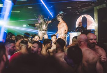 Aqua Club, a gay cruise club in Torremolinos, Spain. Party scene with shirtless men and performers in costumes under blue and green lights.