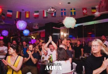 Aqua Club gay cruise club in Torremolinos. Cheering crowd at Terrazza Aqua, a popular gay bar. Flags and festive lights decorate the space.