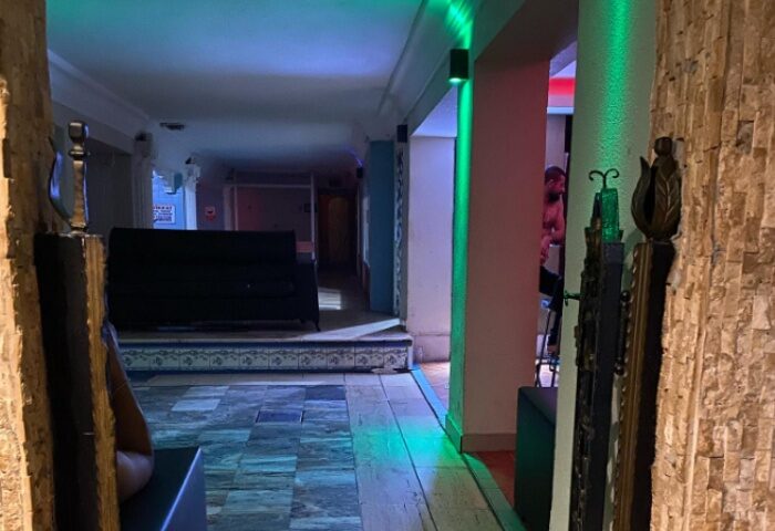 Aquarius Sauna Istanbul interior. Hallway view with stone walls, green lighting, and a glimpse of a man inside. Gay sauna travel advice.