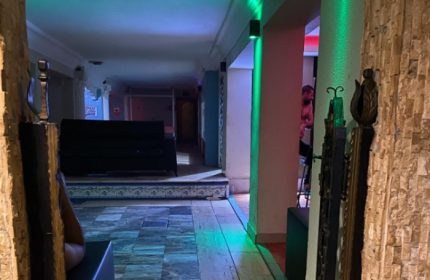 Aquarius Sauna Istanbul interior. Hallway view with stone walls, green lighting, and a glimpse of a man inside. Gay sauna travel advice.