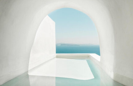 Armenaki Santorini rooftop pool view. Coolest gay hotels in Santorini, Greece. White archway framing the Aegean Sea. Minimalist design.
