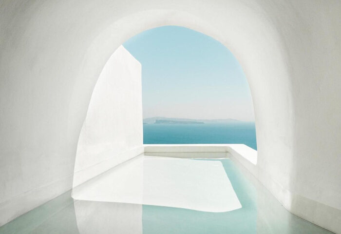 Armenaki Santorini rooftop pool view. Coolest gay hotels in Santorini, Greece. White archway framing the Aegean Sea. Minimalist design.