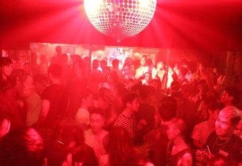 Arty Farty Tokyo's gay dance club. Red lighting illuminates a crowded dance floor with a disco ball. Popular gay nightlife in Tokyo.