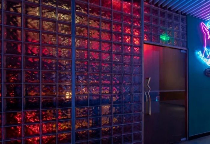 Shanghai gay bar entrance with glass block wall, neon sign, and door. Nightlife scene for gay men traveling in Asia. Blue and red lighting.