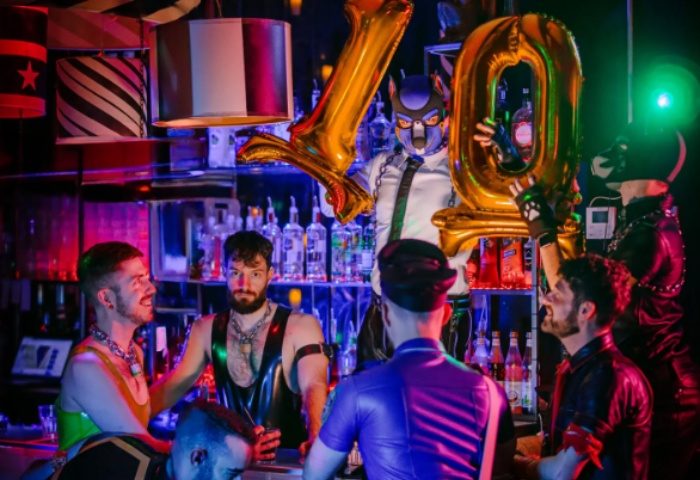 Bangalov Milano gay event: Men in fetish gear celebrate at a bar with balloons. Gay travel in Milan's nightlife scene.
