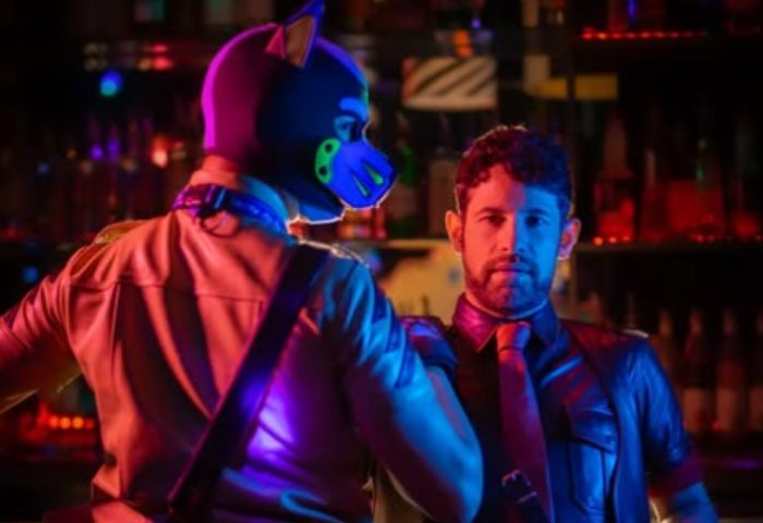 Bangalov Milano: Gay bar scene with a man in a puppy mask and another in leather, standing in front of a bar with colorful lights.