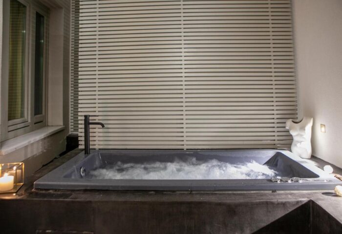 Athens 1890 Hotel & Spa adults only: Gay-friendly hotel spa tub with bubbles, window, blinds, candle, and male torso statue.