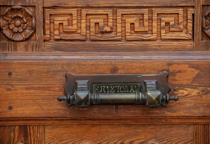 Athens 1890 Hotel door detail. Carved wood with Greek key pattern and flower, plus vintage mail slot. Gay-friendly hotel in Athens.
