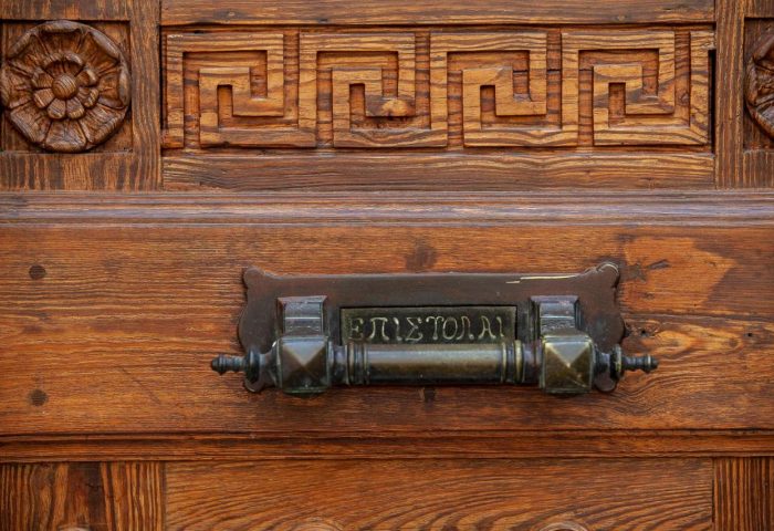Athens 1890 Hotel door detail. Carved wood with Greek key pattern and flower, plus vintage mail slot. Gay-friendly hotel in Athens.
