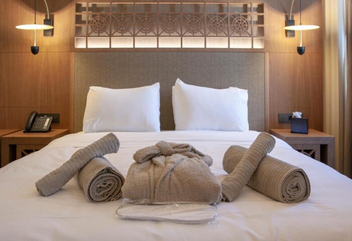Athens 1890 Hotel bedroom. Adults-only gay-friendly hotel with robe, towels, and slippers on a king-size bed. Spa amenities for gay travelers.