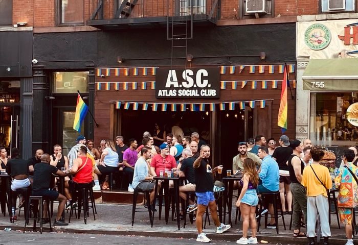 Atlas Social Club in New York. Gay bar scene with rainbow flags. People socializing at the outdoor tables. Gay travel destination.