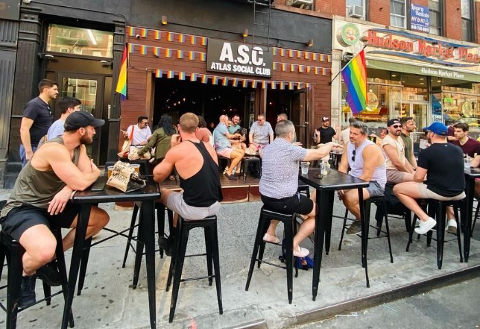 Atlas Social Club in New York City: Gay men gather outside, enjoying drinks. Rainbow flags adorn the popular gay bar. Gay travel advice.