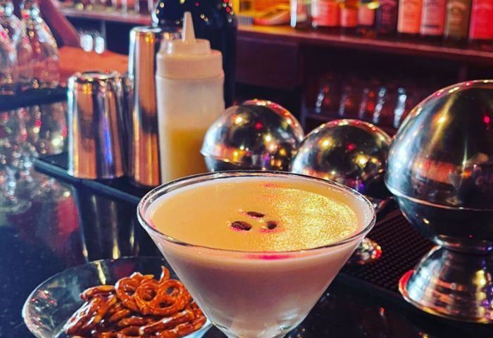 Atlas Social Club in New York: Cocktail in a martini glass with pretzels, bar tools, and shiny metal spheres. Gay bar scene.