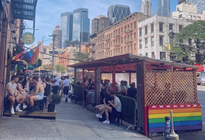 Atlas Social Club in New York: Outdoor seating area with gay men, rainbow flag, and city skyline. Gay travel advice.