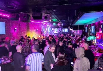 Atmosphere gay bar in Andersonville, Chicago. Patrons enjoy live music in a crowded, colorful space with exposed brick and disco balls.