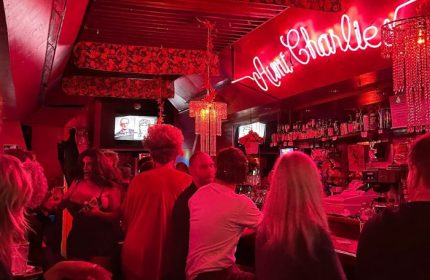 Aunt Charlie's Lounge, San Francisco. A neon sign glows above patrons at this popular gay bar. Red lighting and chandeliers add to the ambiance.