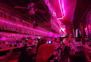 Interior of Aunt Charlie's Lounge in San Francisco. Pink lighting, tinsel decor, and patrons at the bar create a vibrant, gay-friendly atmosphere.