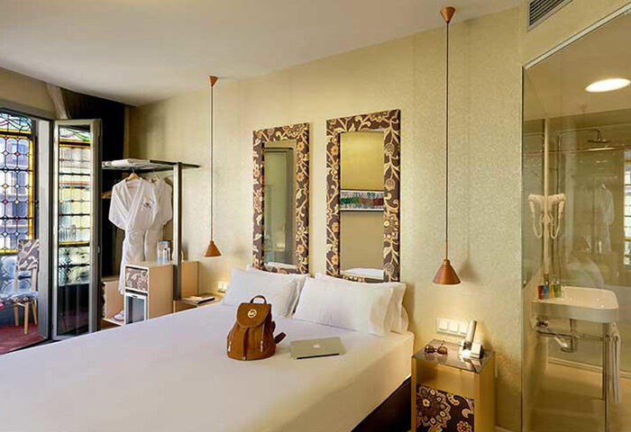 Axel Hotel Barcelona room. Gay adults-only hotel near gay bars. Room with bed, backpack, laptop, mirrors, and bathroom. Urban spa hotel.