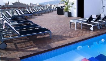 Axel Hotel Barcelona rooftop pool. Gay adults only hotel. Deck chairs line the wooden deck overlooking the city. Most booked gay hotel.