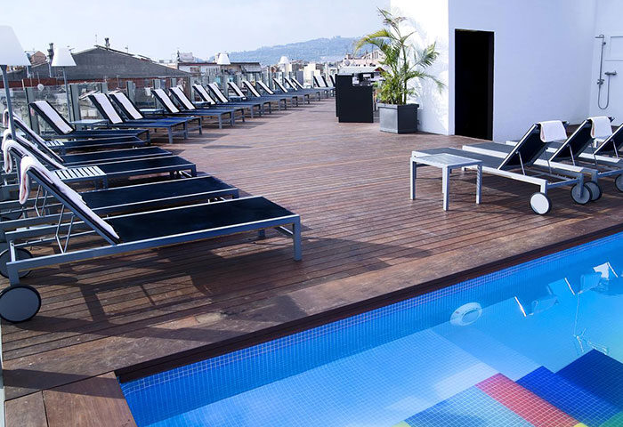Axel Hotel Barcelona rooftop pool. Gay adults only hotel. Deck chairs line the wooden deck overlooking the city. Most booked gay hotel.