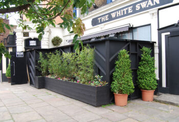 BJ's White Swan Gay Club, London. Exterior view of the pub with black fencing and greenery, popular gay travel destination.