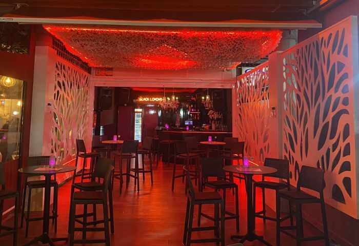 Interior of Black Lomond Bar, a gay bar in Gran Canaria. Tables and chairs under red lighting, stylish decor.