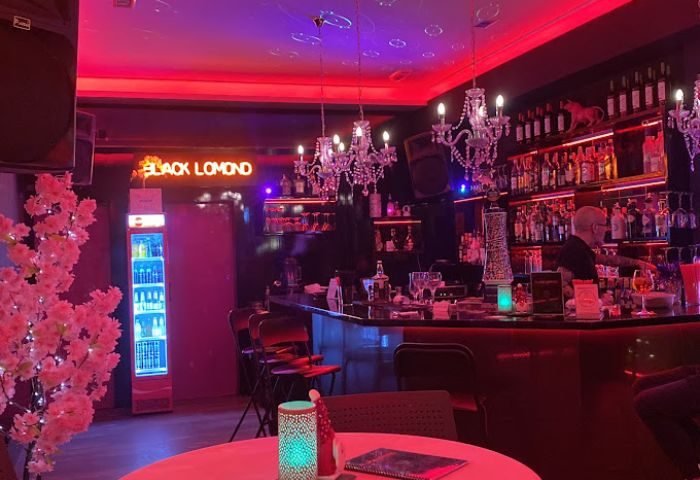Interior of Black Lomond Bar, a gay bar in Gran Canaria. Red lighting, chandeliers, and a well-stocked bar create a vibrant atmosphere.