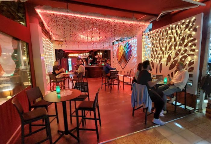 Interior of Black Lomond Bar, a gay bar in Gran Canaria. Patrons sit at tables, enjoying drinks in the atmospheric, warmly lit space.