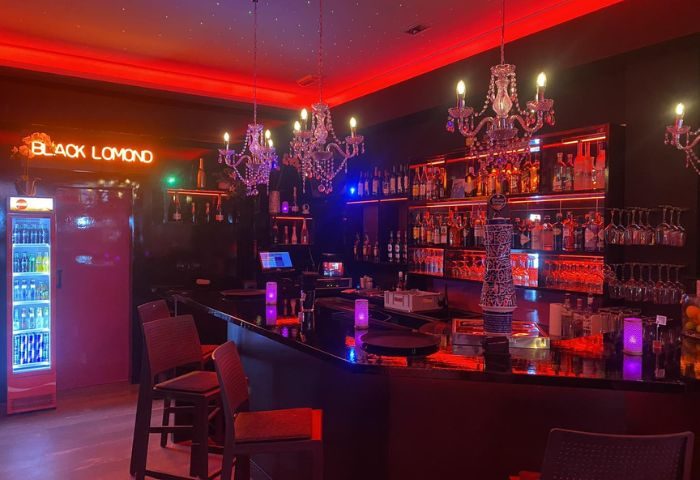 Black Lomond Gay Bar in Gran Canaria. Interior view of the bar area with chandeliers, shelves of liquor, and red lighting.