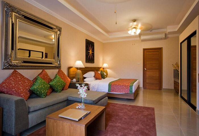 Baan Souy Resort's exclusive gay hotel room. Features a bed, couch, mirror, and table. Ideal for gay travel and relaxation.