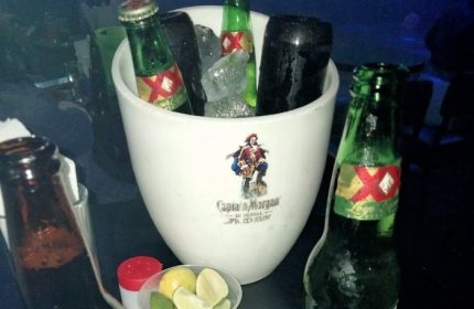 Ice bucket with XX Lager at a gay bar in Mexico. Limes and salt are nearby. Captain Morgan logo on bucket. Gay travel advice.
