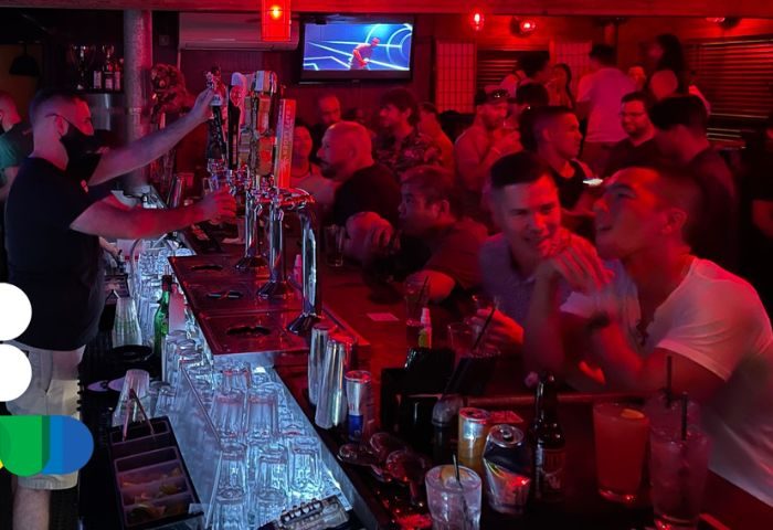 Bacchus Waikiki gay bar party in Honolulu. Bartender serving drinks at a crowded bar. Gay nightlife in Hawaii. Men socializing, red lights.