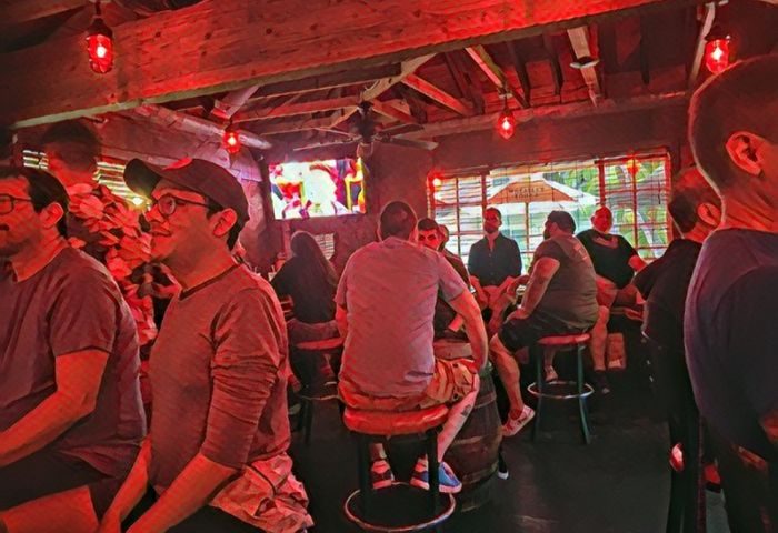 Inside Bacchus Waikiki gay bar in Honolulu. Men at bar stools, red lighting, and a TV screen. Popular gay party spot.