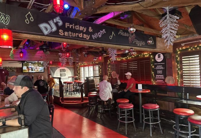 Interior of Bacchus Waikiki gay bar in Honolulu. DJ's Friday & Saturday nights. Red stools, bar, and patrons. Gay travel advice.