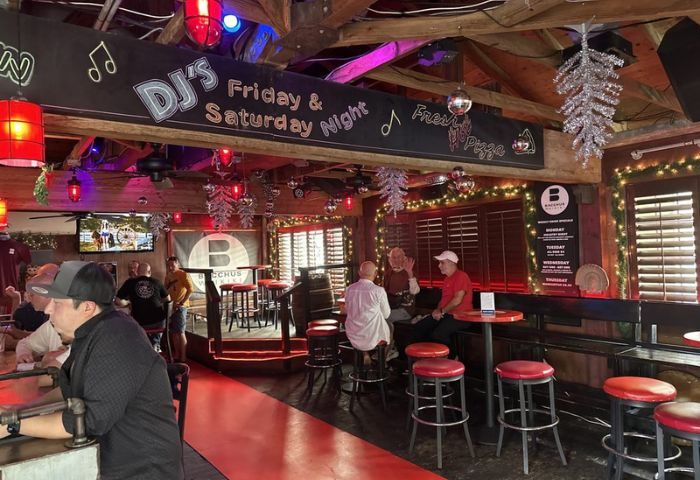 Interior of Bacchus Waikiki gay bar in Honolulu. DJ's Friday & Saturday nights. Red stools, bar, and patrons. Gay travel advice.