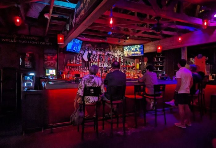 Bacchus Waikiki gay bar in Honolulu, a party spot. People at the bar, red lighting, TVs, and a lively atmosphere. Travel advice for gay men.