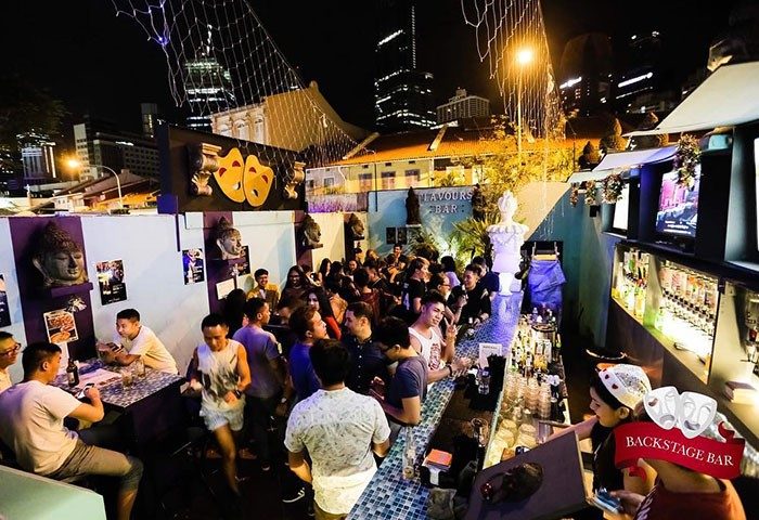 Backstage Bar Singapore, a rooftop gay bar in Chinatown. Crowded scene with men at the bar and tables, enjoying the nightlife. Night view.