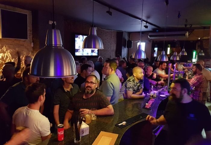 Busy Bacon Bear Bar in Barcelona. Gay bar scene with many men at the bar, drinking, socializing. Travel advice for gay men.