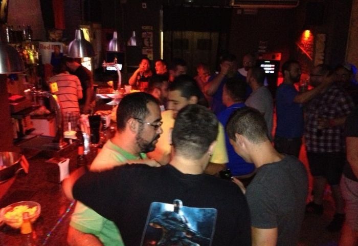 Inside Bacon Bear Bar, a gay bar in Barcelona. Men gather, some at the bar, others in conversation, creating a lively, social atmosphere.