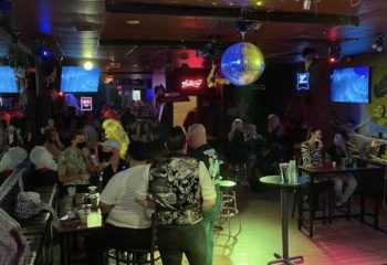 Interior shot of Badlands Las Vegas, a popular gay bar. People are socializing, with a disco ball and neon signs enhancing the atmosphere.
